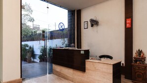 A reception area with a glass door, a reception desk, a wall-mounted fan, and a small shrine. - OYO 644 Hotel Haris Court (Gurugram)