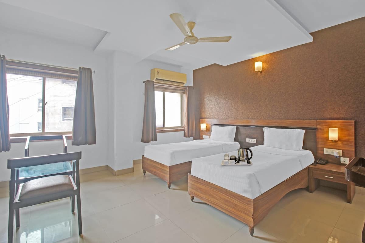 A hotel room with two beds, a desk, a chair, a ceiling fan, and a window with curtains.