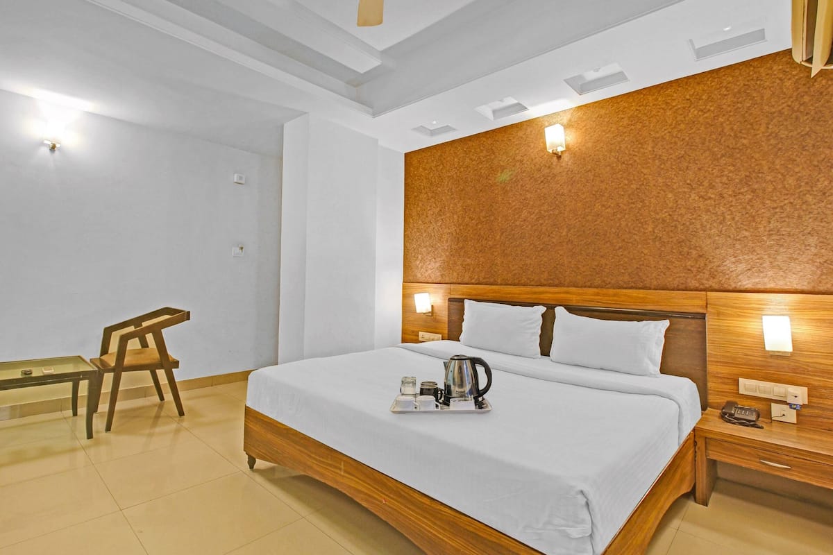 A hotel room with a wooden bed, bedside tables, a nightstand, a chair, and a small table with a tray of items.