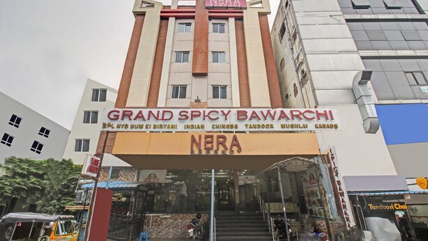 Un bâtiment dont la façade porte une enseigne indiquant « Grand Spicy Bawarchi » et « NERA ».