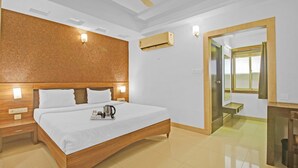Une chambre d’hôtel avec un lit en bois, une table de chevet, un climatiseur fixé au mur et une porte donnant sur une salle de bain.