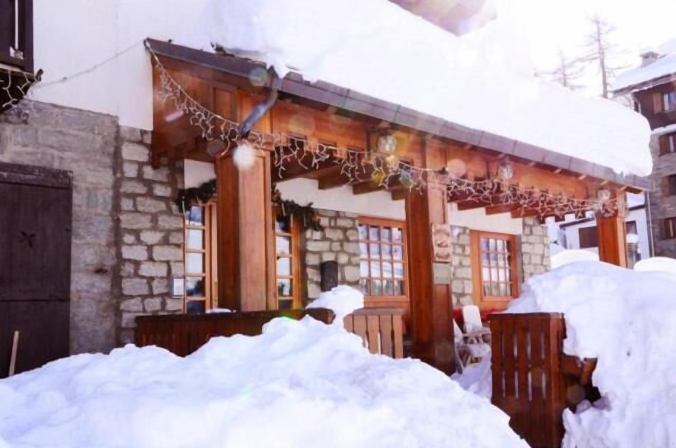 Ein Steinhaus mit einer Holzveranda und einem mit Schnee bedeckten Dach.