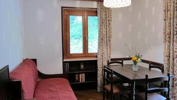 Une pièce confortable avec un lit, une télévision, une table à manger avec des chaises et une fenêtre avec des rideaux.
