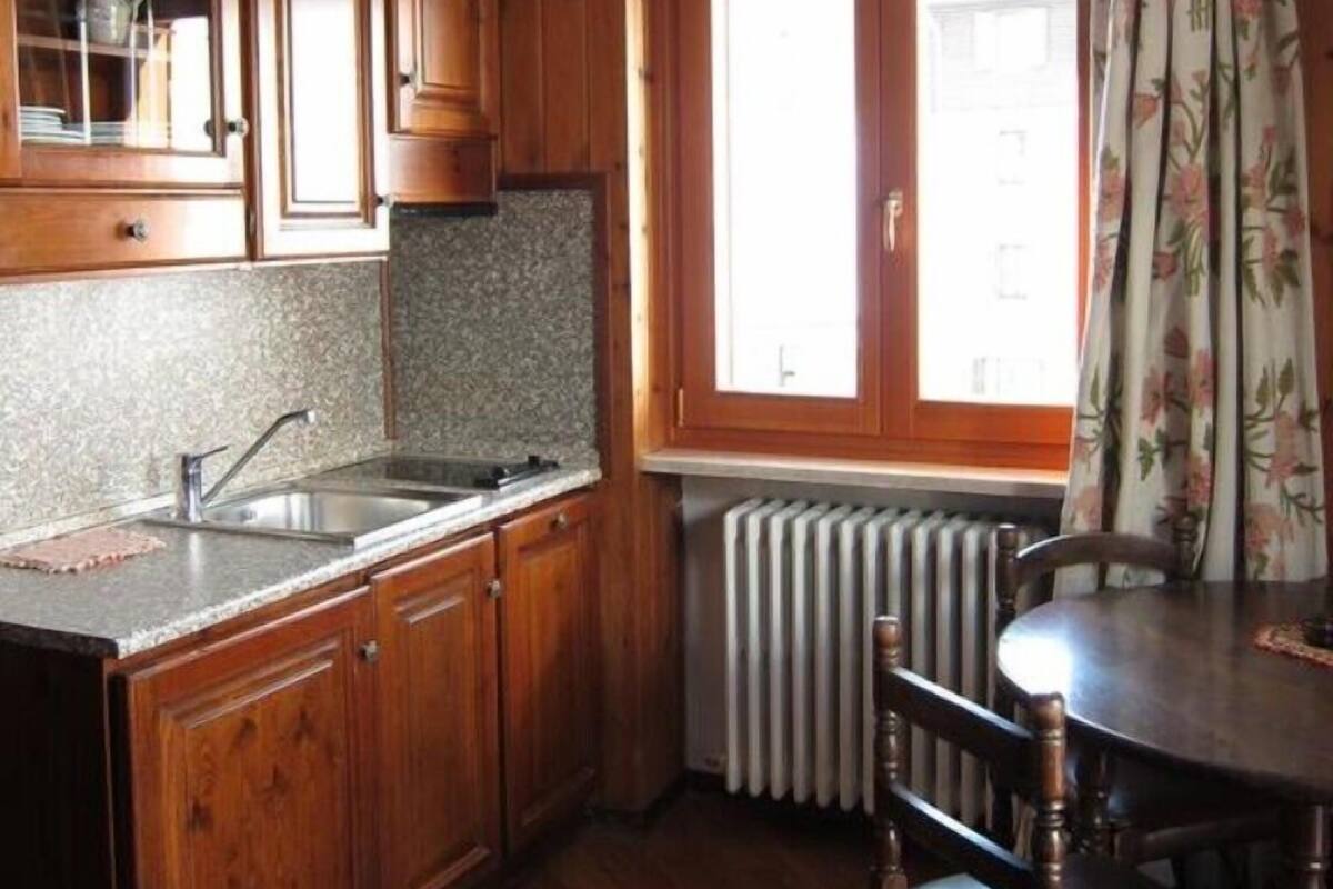 Una cocina con armarios de madera, encimera de granito, fregadero, ventana con cortina floral y radiador.