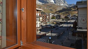 A view from a window with a wooden frame, overlooking a town with buildings and a mountain in the background. - Residence Castelli (Valtournenche)