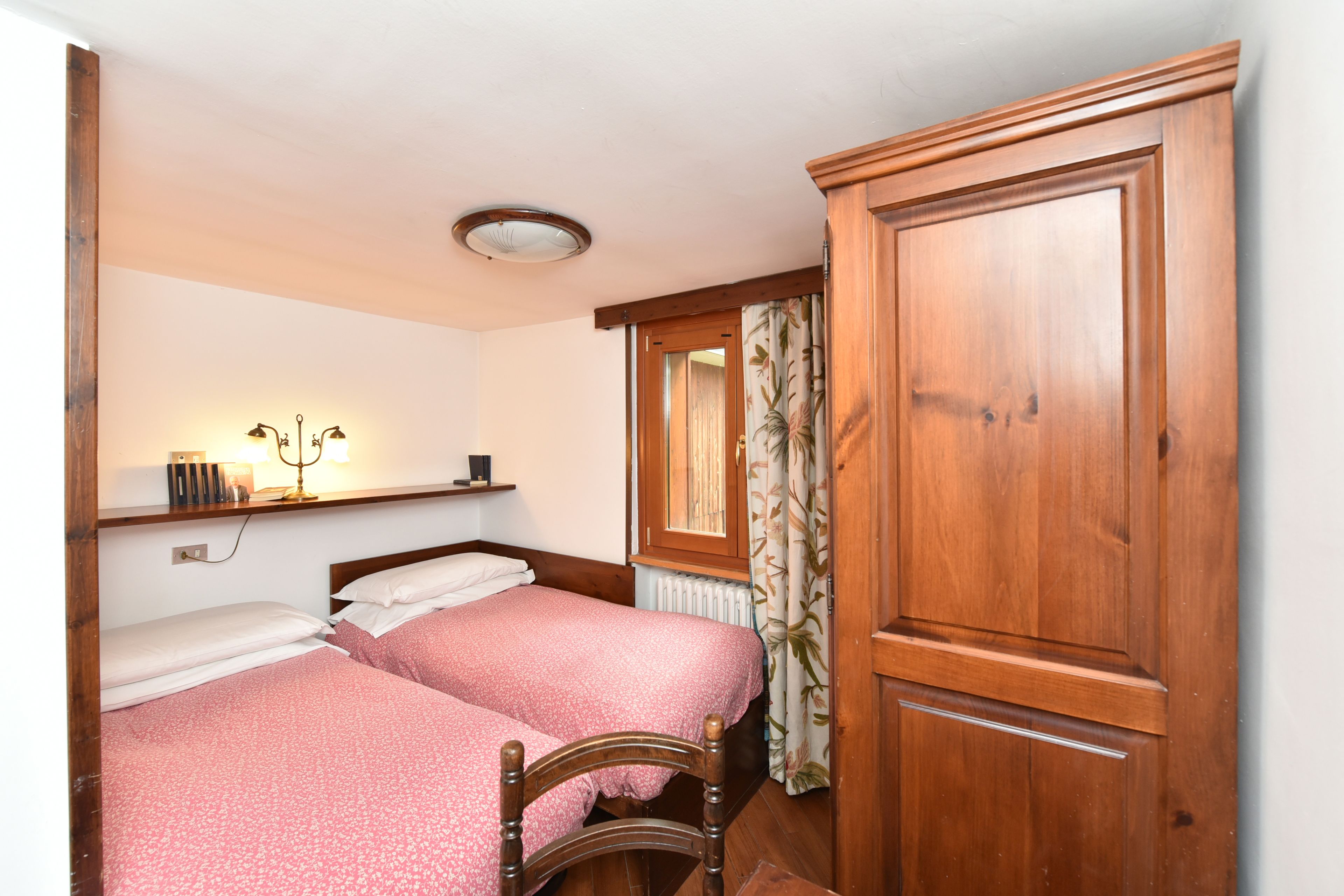 Une chambre avec deux lits, une armoire en bois et une étagère avec des livres et une lampe.