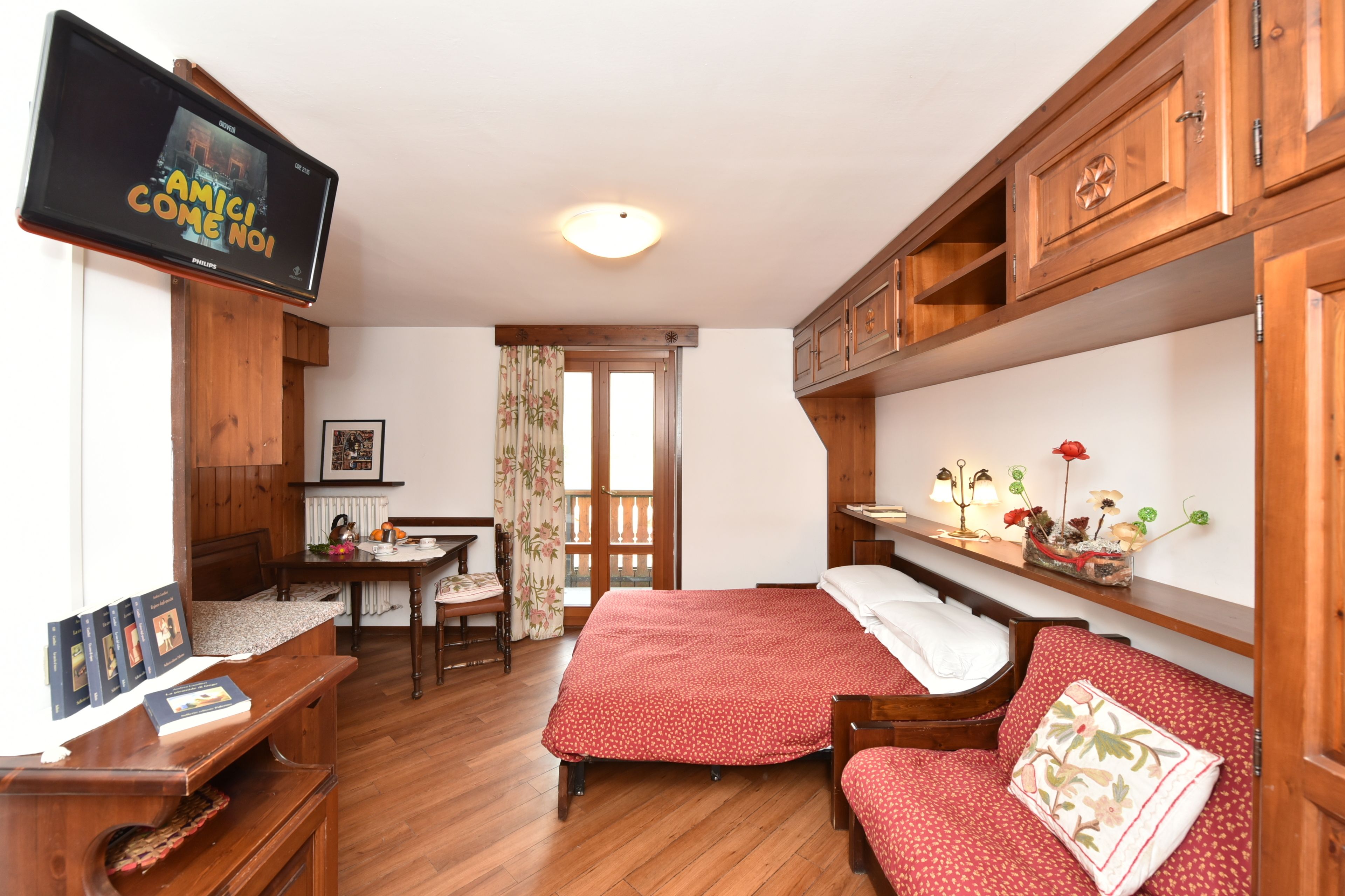 Ein gemütliches Zimmer mit einem Bett, einem Schreibtisch, einem Fernseher und Holzsärchen.