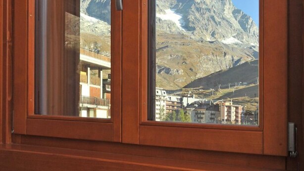 A wooden-framed window with a view of a mountain and buildings. - Residence Castelli (Valtournenche)