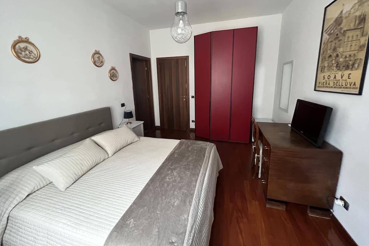 A bedroom with a bed, a wardrobe, a desk, and a television.
