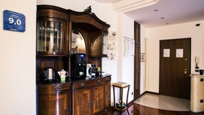A wooden cabinet with a coffee maker, a kettle, and a mug. There is a small table with a bowl and a cup. A door with a sign is visible in the background. - 10 Minutes B&B (Verona)