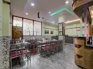 A restaurant with marble flooring, wooden chairs, and tables. There is a ceiling fan and a hand wash station.