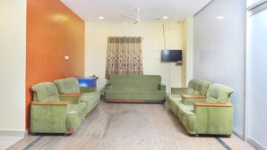 A room with two green sofas, a television on a stand, and a patterned curtain. - OYO 12765 Hotel Golden Rooms (Tirupati)