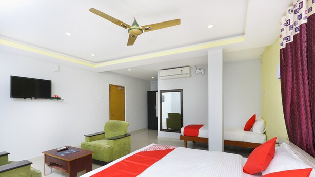 A hotel room with a bed, a green armchair, a small table, a television, and a ceiling fan. - OYO 12765 Hotel Golden Rooms (Tirupati)