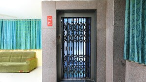 An elevator with a metal grille door, a green sofa, and blue patterned curtains. - OYO 12765 Hotel Golden Rooms (Tirupati)