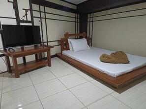 Un dormitorio con una cama de madera, un televisor sobre un mueble de madera y un suelo de baldosas.