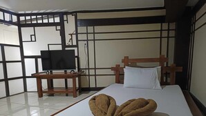 A hotel room with a bed, a wooden nightstand with a television, and a decorative wall panel. - Vista de Pino (Baguio)