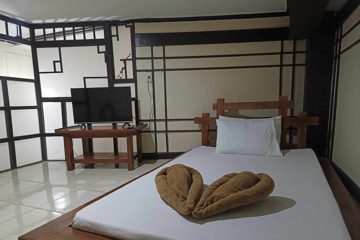Een hotelkamer met een bed, een houten nachtkastje met een televisie, en een decoratief wandpaneel.
