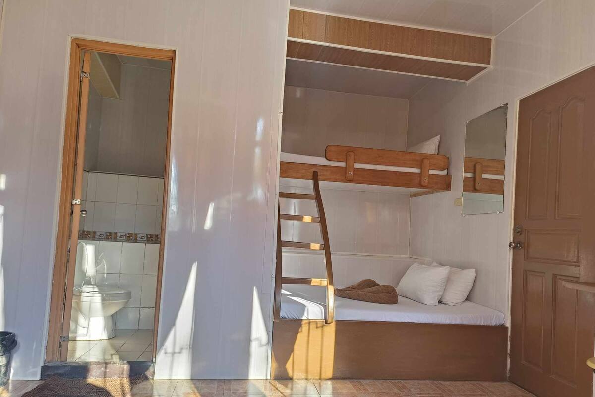 Een compacte kamer met een stapelbed, een houten trapje, een klein nachtkastje en een deur naar een badkamer.