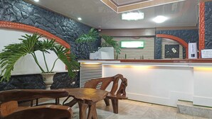 A reception area with a marble wall, wooden chairs, a reception desk, and potted plants. - Vista de Pino (Baguio)