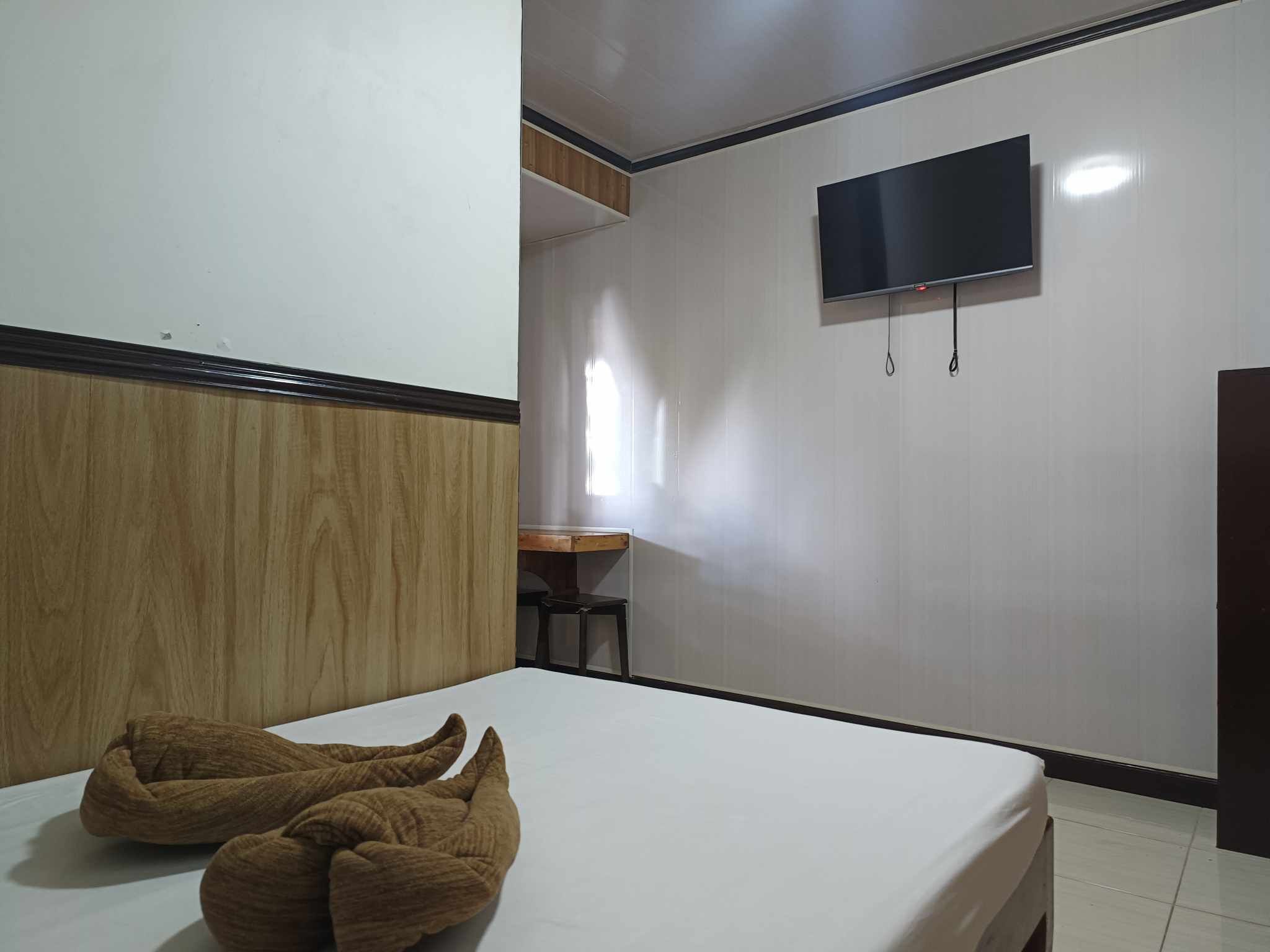 A hotel room with a bed, a TV mounted on the wall, and a wooden headboard.