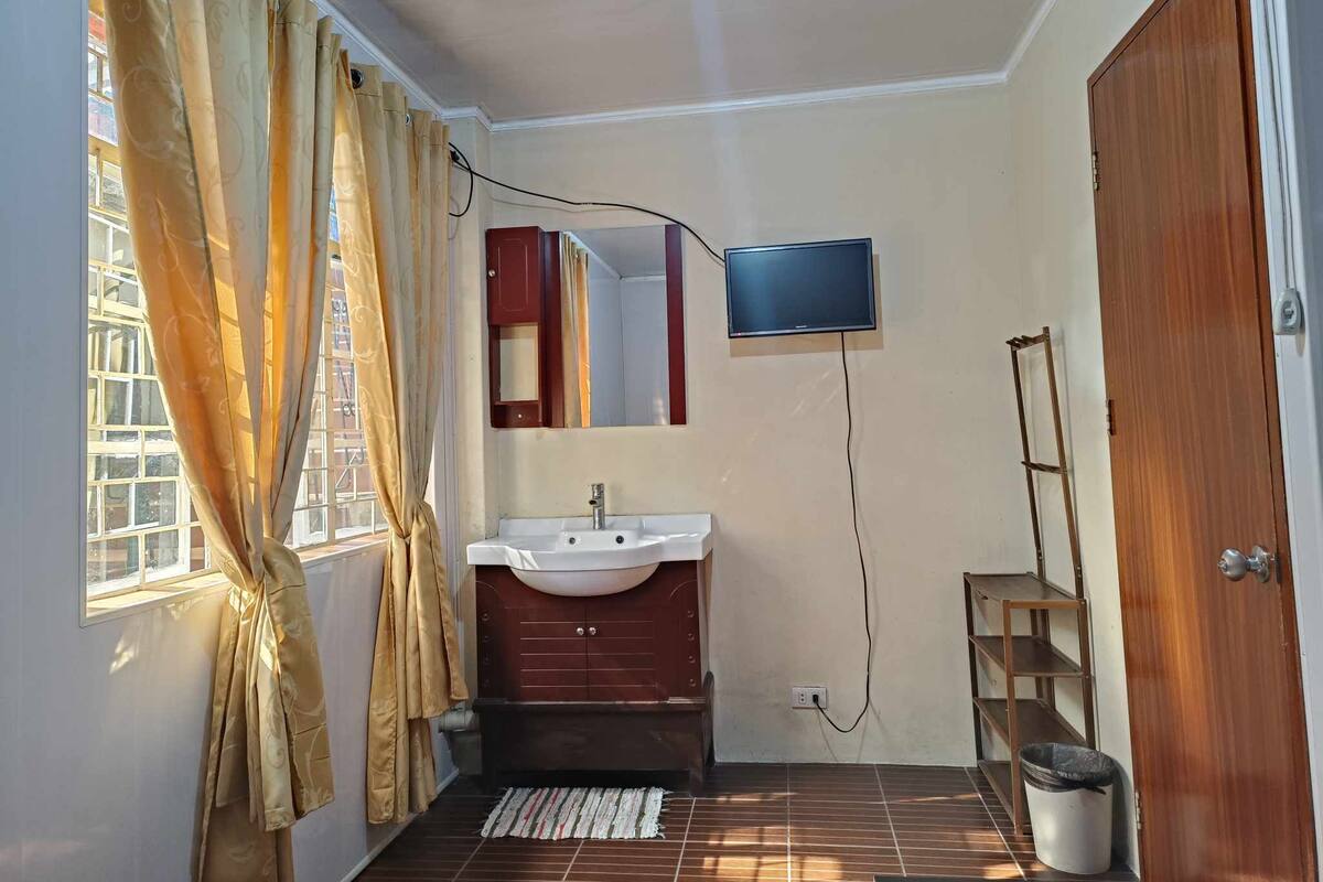 Een kleine badkamer met een wastafel, spiegel en een televisie aan de muur.