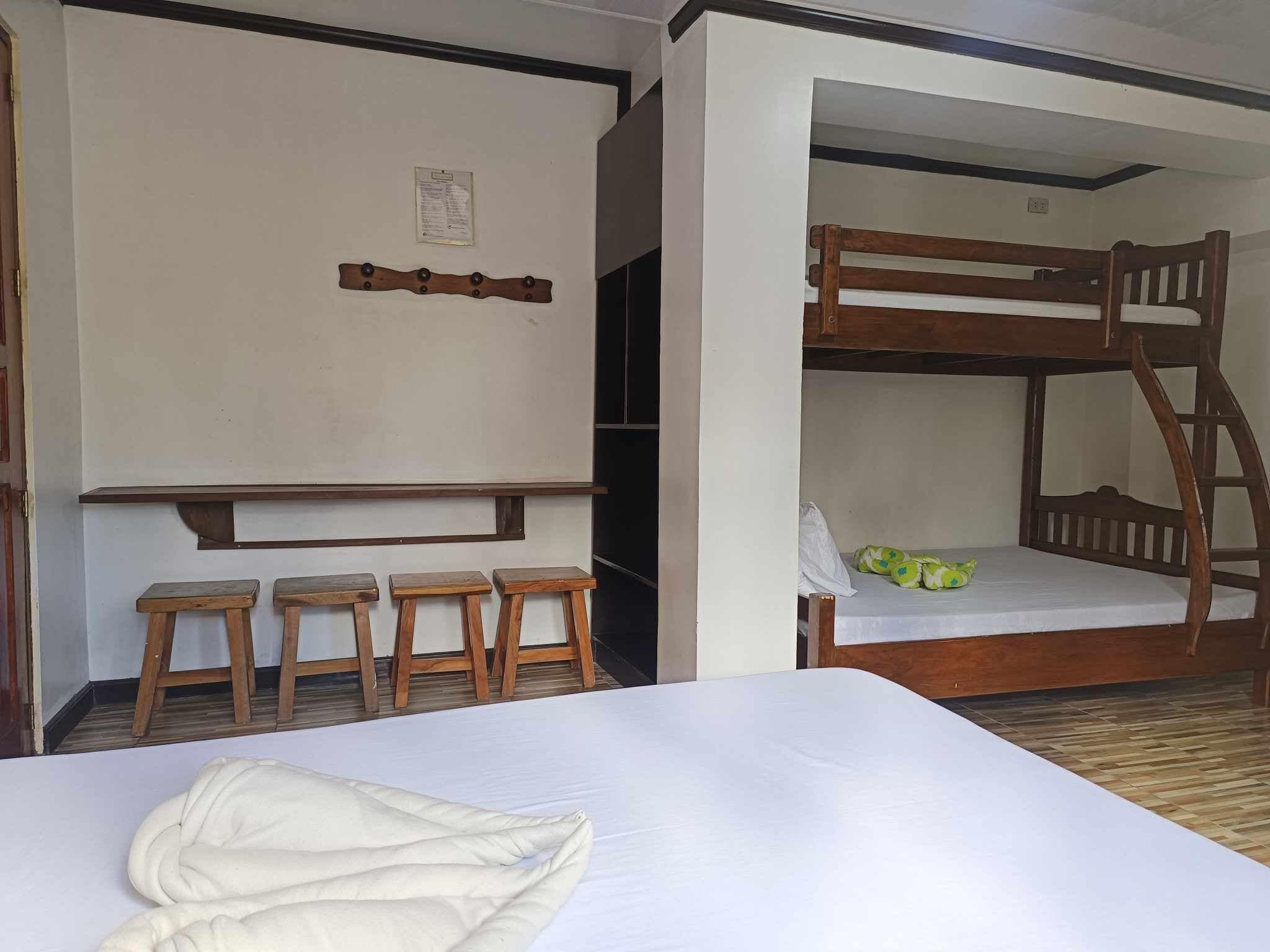 A bunk bed room with a bunk on top and a lower bunk. There are two wooden stools and a white bedspread.