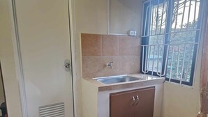 A small kitchen with a sink, a window with bars, and a door with a vent. - Vista de Pino (Baguio)