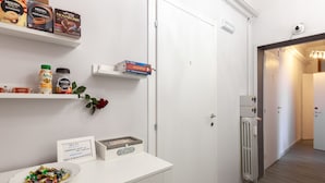 A hotel room with a white door, a radiator, a shelf with books and coffee products, a bowl of candies, and a framed note on the counter. - Heart of San Lorenzo (Rome)