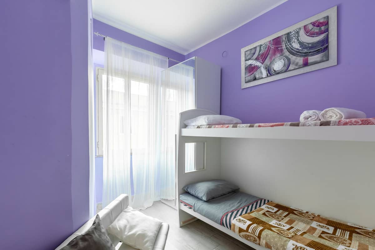 A bunk bed room with a window, a couch, and a painting on the wall.