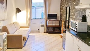 A compact living space with a sofa, a television, a kitchenette, and a window with curtains. - Heart of San Lorenzo (Rome)