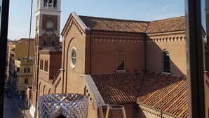 A view of a historic building with a bell tower and arched windows, viewed from a window with a decorative glass object and two wine glasses on the sill. - Heart of San Lorenzo (Rome)