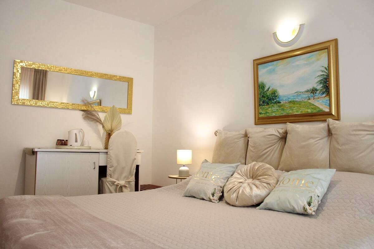 A hotel room with a bed, a desk, a chair, a lamp, a painting, and a mirror.