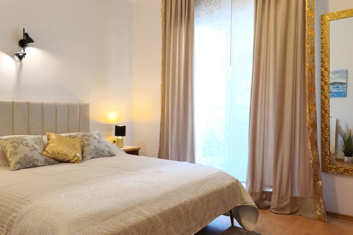 A bed with a headboard, a bedside lamp, a decorative pillow, and a mirror with a gold frame.