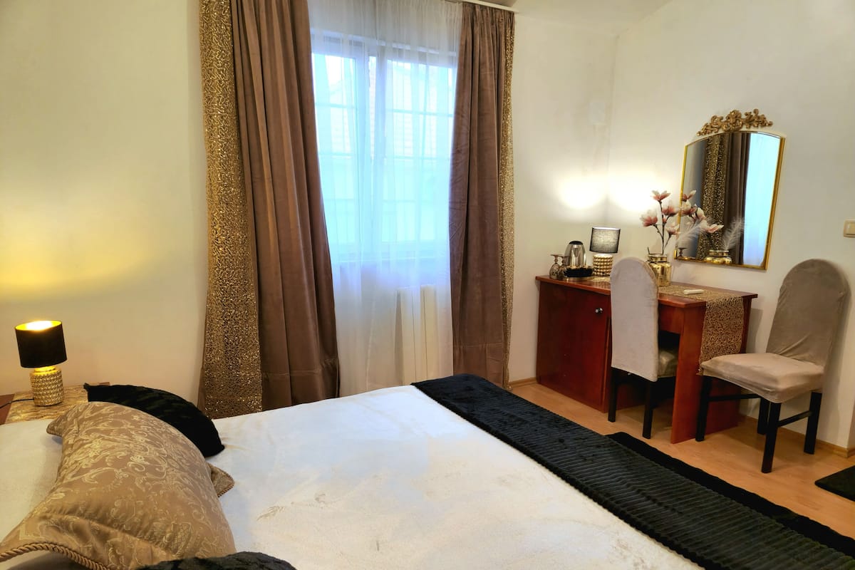 A hotel room with a bed, a desk, a chair, a lamp, and a mirror.