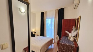 A hotel room with a bed, a desk with a chair, a mirror, and a window with curtains. - Avalena Rooms (Zadar)
