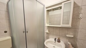 A bathroom with a glass-enclosed shower, a sink with a mirror above it, and a towel hanging on the wall. - Avalena Rooms (Zadar)