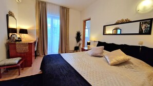 A hotel room with a bed, a desk, a chair, a mirror, and a window with curtains. - Avalena Rooms (Zadar)