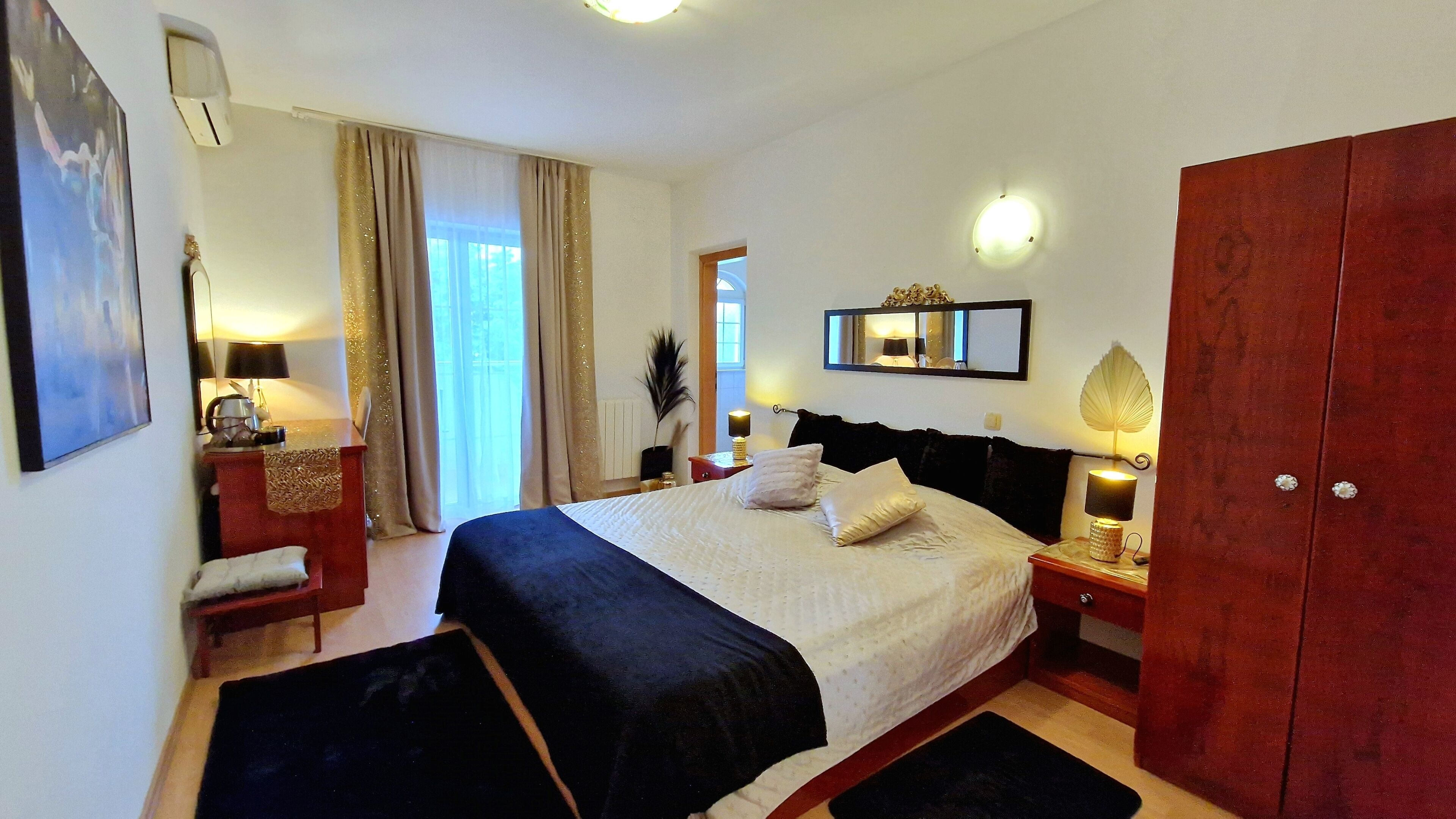 Un dormitorio con cama, mesitas de noche, armario, espejo y ventana con cortinas.