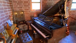A room with a grand piano, a smaller keyboard, a drum set, and a speaker. - Okinawa starry forest cottage (Onna)