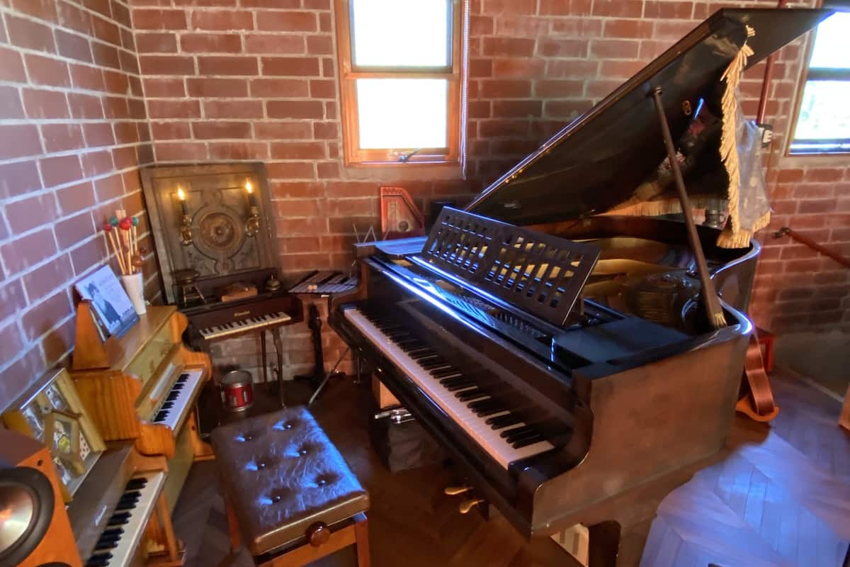 A room with a grand piano, a smaller keyboard, a drum set, and a speaker.