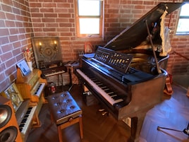 A room with a grand piano, a smaller keyboard, a drum set, and a speaker.
