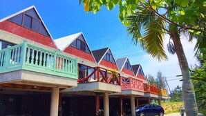 A row of multi-story buildings with balconies, a car parked in front, and a palm tree. - Okinawa starry forest cottage (Onna)