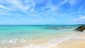 A beach with clear turquoise water, a sandy shore, and a rocky outcrop. - Okinawa starry forest cottage (Onna)