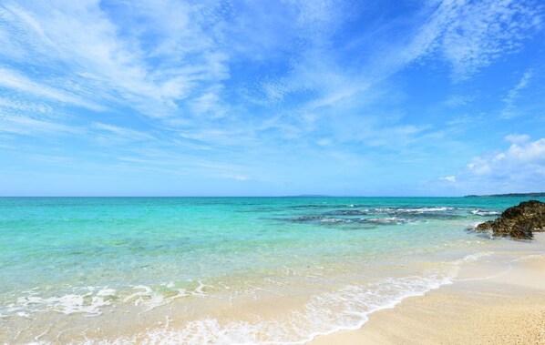 Uma praia com águas azul-turquesa cristalinas, areal arenoso e um afloramento rochoso.