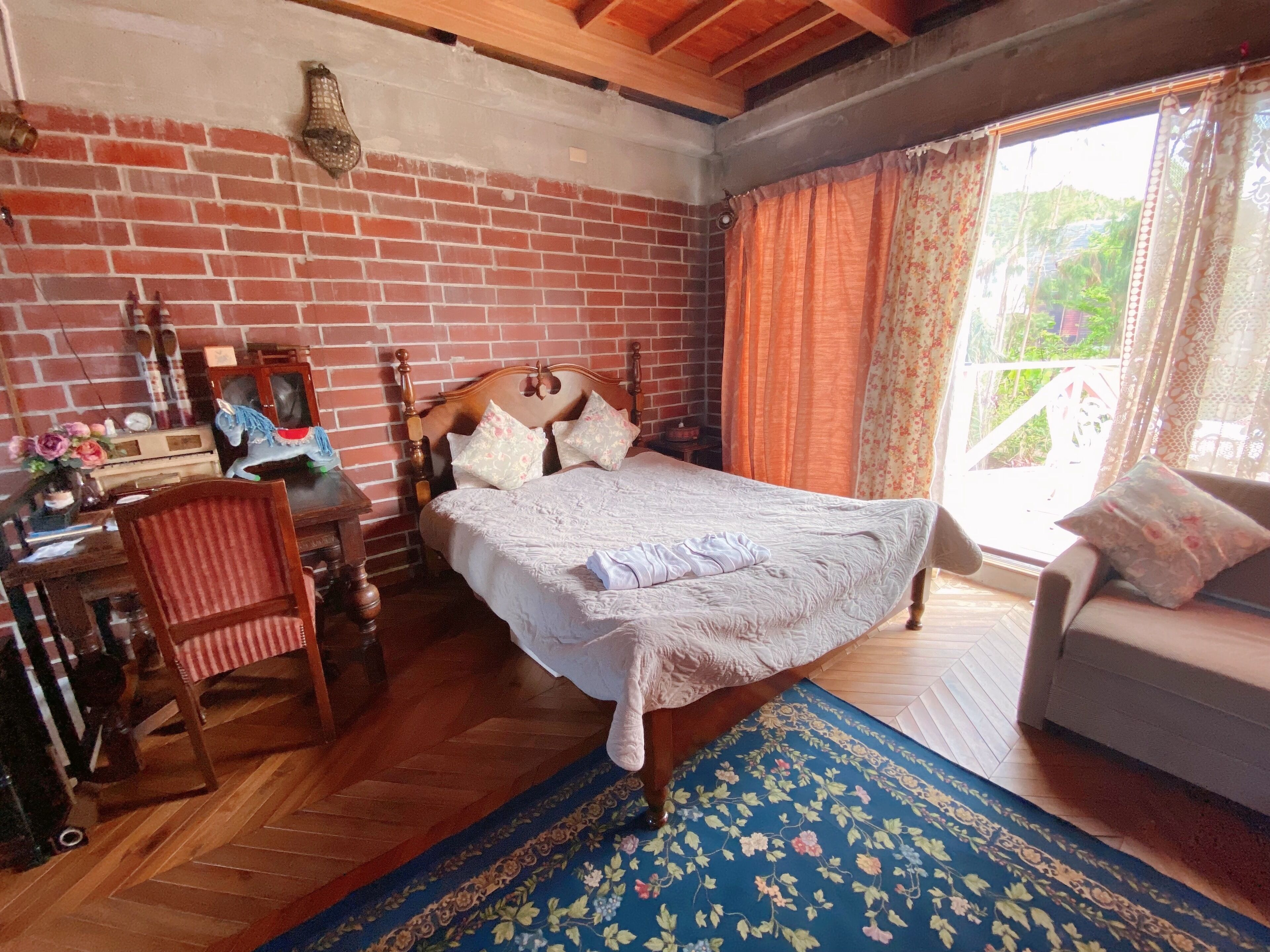 Camera da letto con parete in mattoni, struttura del letto in legno e un'ampia finestra con tende.