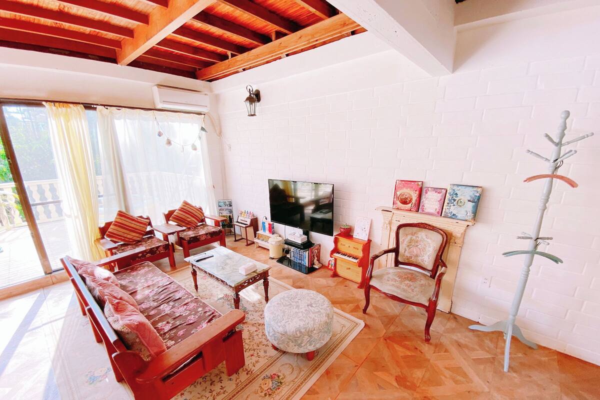 A living room with a sofa set, a television, a piano, and a fireplace.