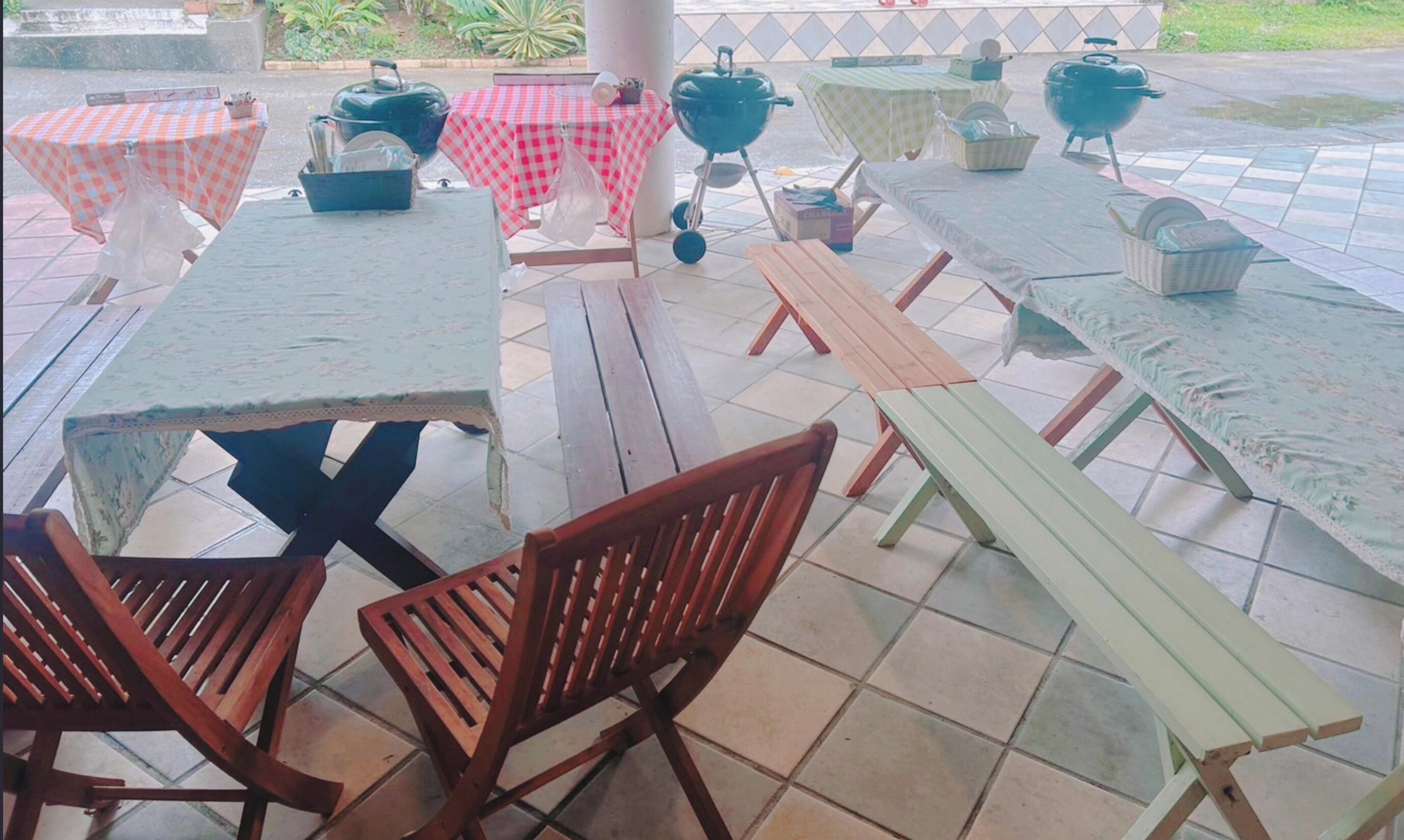 An outdoor patio with several tables and benches, some covered with checkered tablecloths.
