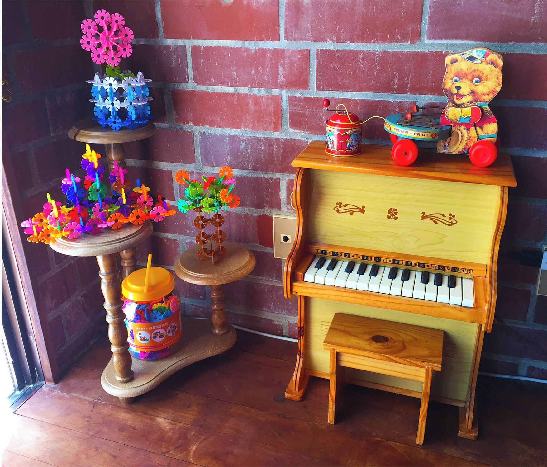 A small wooden piano with a bear figurine on top, a toy train, and a colorful flower arrangement on a stand.