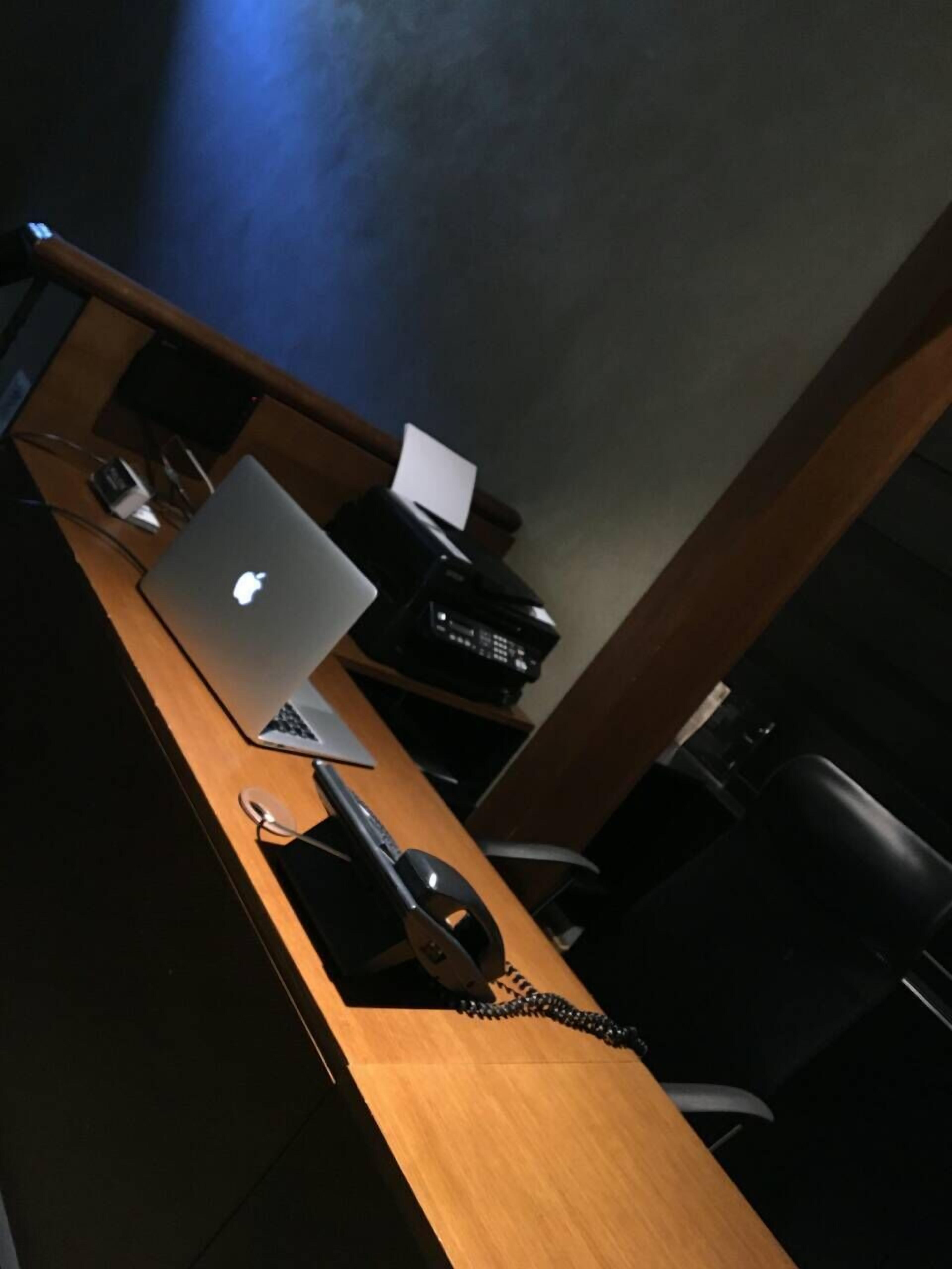 A wooden desk with a laptop, a printer, and a telephone.