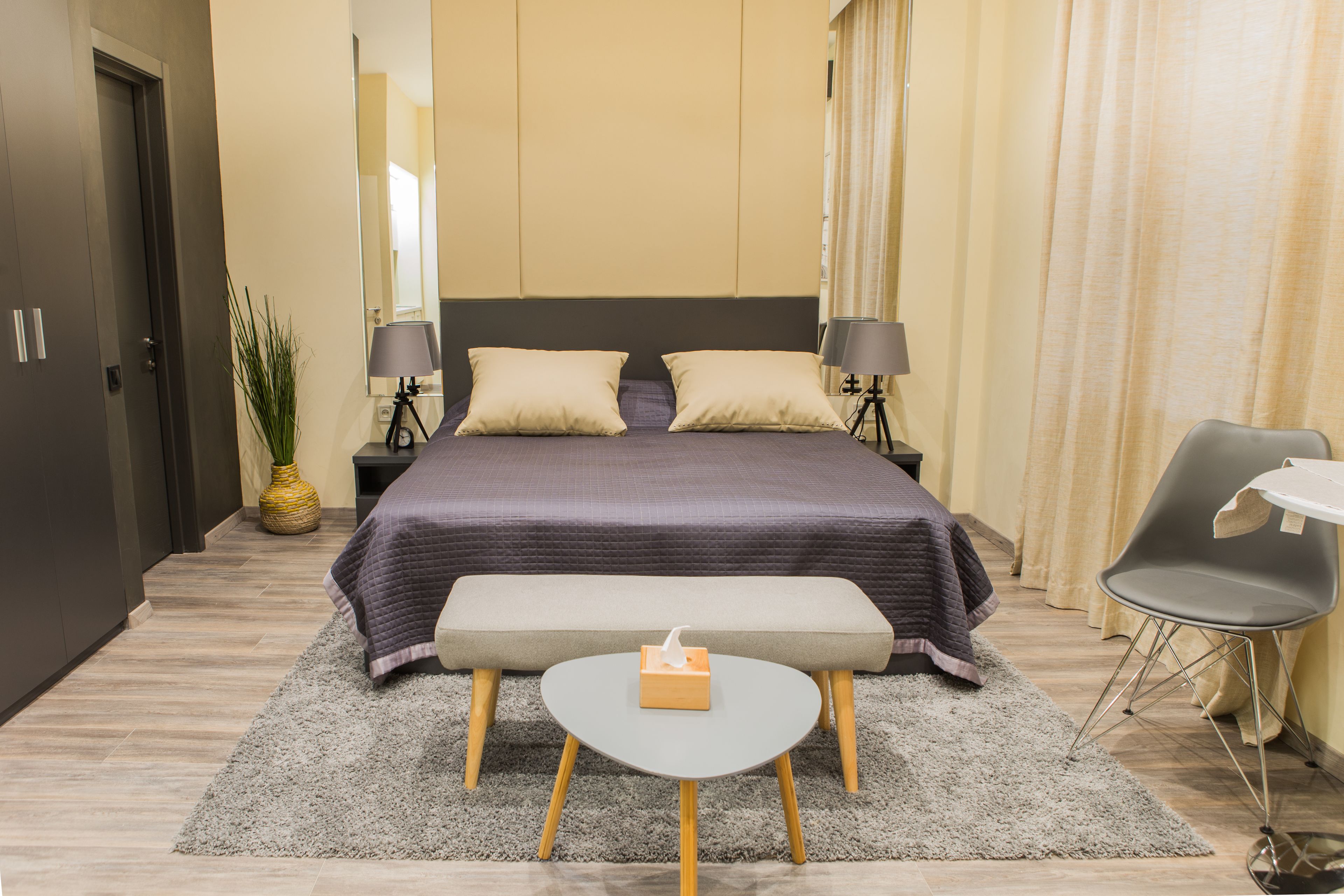 A neatly arranged bedroom with a bed, bedside lamps, a small table, and a chair.